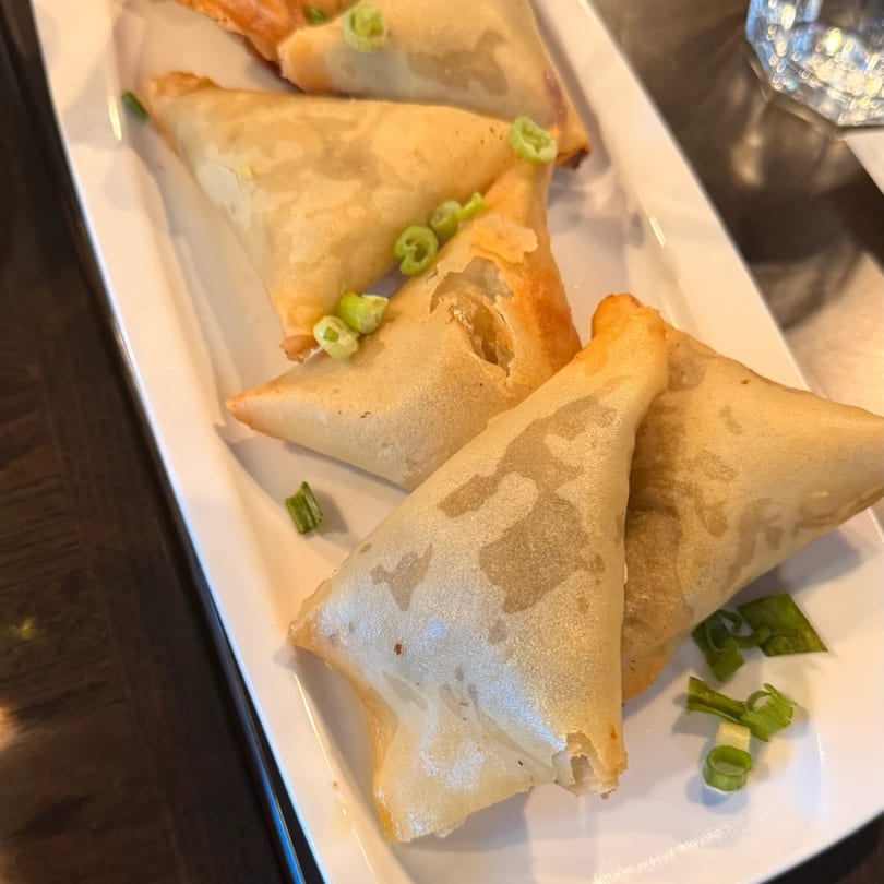 Crispy Bangladeshi samosas, triangular and golden brown, garnished with fresh green onions on a white plate.