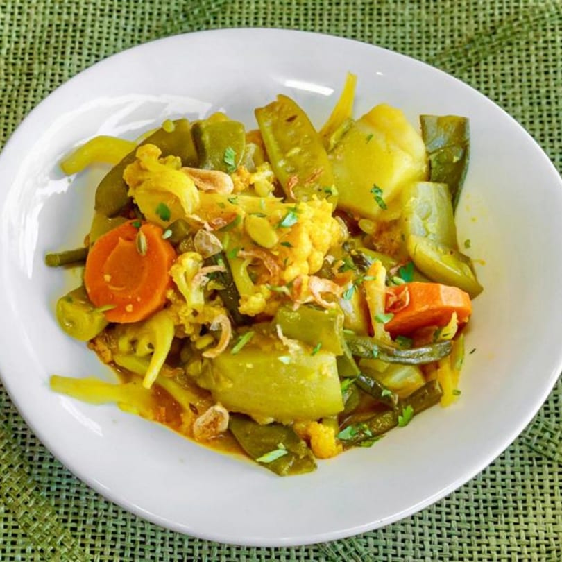 A vibrant Bangladeshi vegetable curry with cauliflower, carrots, potatoes, and green beans on a white plate.