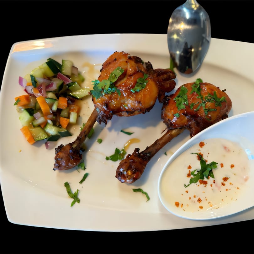 Two glazed chicken drumsticks with a side of cucumber salad and a white dipping sauce.