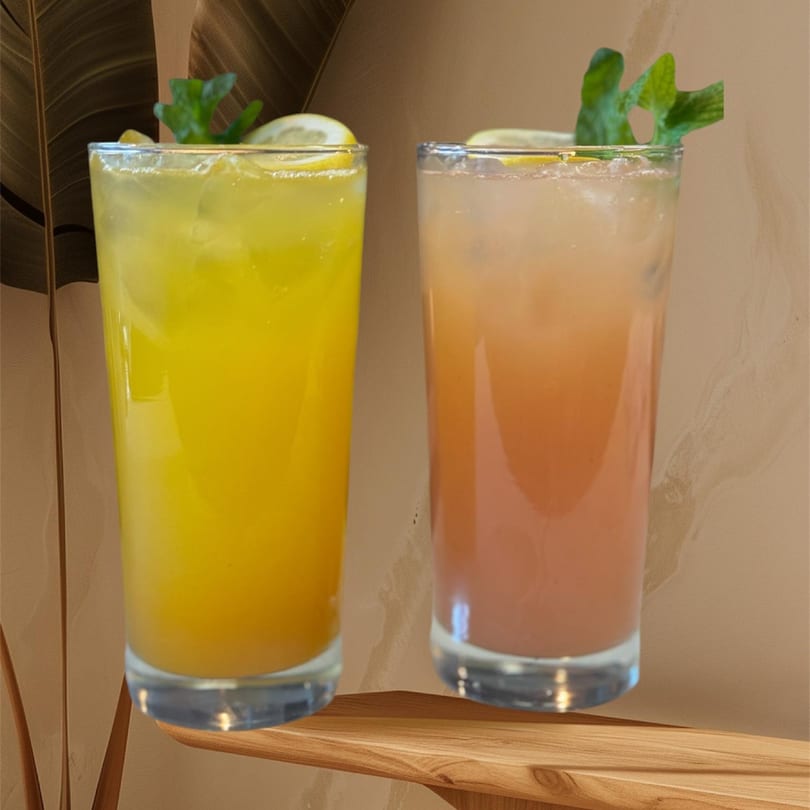 Two refreshing Atithi Restaurant drinks, one yellow and one peach, garnished with lemon and mint.